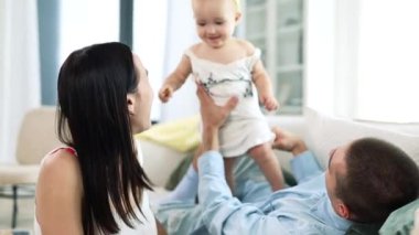 Yumuşak, rahat bir yatak odasında, mutlu, sevgi dolu bin yıllık ebeveynler. Havada küçük bir kız ya da oğlan çocuğu var. Şefkatli anne güler, kucaklar, sevimli bebek öper, iyi eğlenceler..