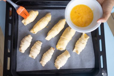 Female baker smears raw croissants with a brush in the yolk, the cooking process.