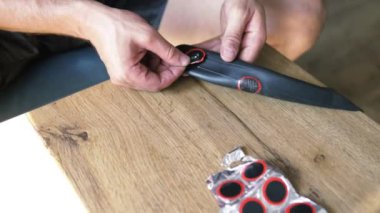 Bir tamircinin yakın çekimi elinde lastik bir yama tutar ve tekerlek iç tüpündeki deliği kapatır. Elektrikli scooter tekerleği için lastik lastiğin değiştirilmesi. Tekerlekler atölyede sökülüp onarılıyor