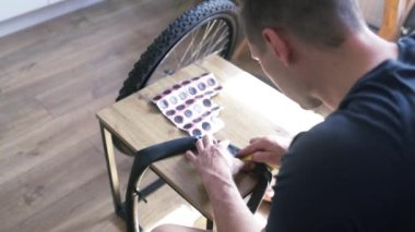 Bir tamircinin yakın çekimi elinde lastik bir yama tutar ve tekerlek iç tüpündeki deliği kapatır. Elektrikli scooter tekerleği için lastik lastiğin değiştirilmesi. Tekerlekler atölyede sökülüp onarılıyor