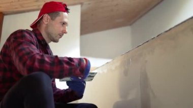 Kafkasyalı genç bir adam müteahhit şeklinde macunu alçıpan dikişine sürüyor. alçı levhaların eklemlerini macunla tamamlamak.