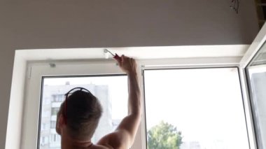 Genç adam beyaz boyalı bir silindirle duvarı boyuyor. Ev tadilatı konsepti, apartmanda tadilat...