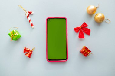 Noel Günü konsepti. Akıllı telefon yıldızının üst görünümü, izole edilmiş mavi arkaplan ve boş alan üzerindeki altın yeşili ve kırmızı mücevherleri süsler.