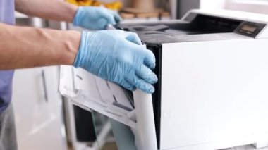 Yazıcı tamircisi. Erkek bir tamirci, müşterisinin dairesinde onarımlara başlamadan önce lazer yazıcıyı kontrol eder..