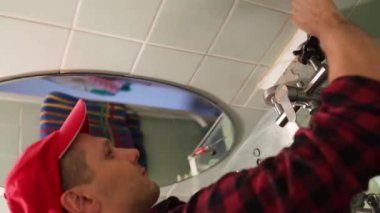 Beyaz erkek tesisatçı lavabodaki sızdıran boruyu tamir ediyor. Banyoda su sızıntısı var..