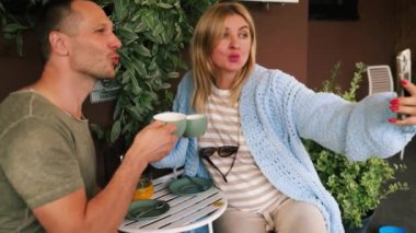 Güneşli bir sonbahar gününde açık havada oturan genç çift. Teras Kafe 'de sipariş bekliyor, akıllı telefon bakıyor, selfie çekiyor..