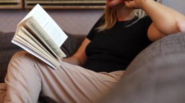 Genç kadın rahat oturma odasında kitap okuyor, öğreniyor, çalışıyor, eğitim görüyor, kitap okuyor, evde kalıp konsept yapıyor..