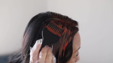 Evde saç boyası. Orta yaşlı bir kadın siyah fırça kullanarak saç boyuyor. Asyalı kadın koyu renk saçlarını yeniden uzamış gri kökleri ile boyuyor.