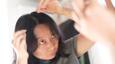 Genç Asyalı kadın aynaya bakarken beyaz saçlarını kontrol ediyor.