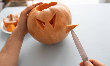 Cadılar Bayramı 'nda balkabağından fener yapma süreci. Adam evde Cadılar Bayramı Balkabağı oyuyor.