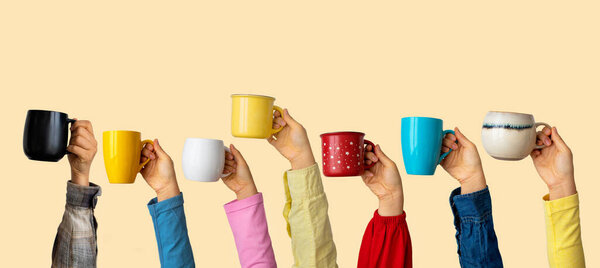 Многие различные руки, держа разноцветные чашки кофе на пастельном фоне. Женские и мужские руки. Концепция дружеской команды, кофе-брейк, встреча с друзьями, утро в команде. Баннер