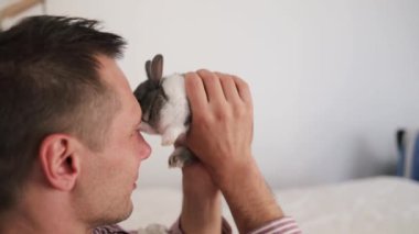 Yatakta sevimli bir tavşanı tutan bir adam. Ev hayvanı. Hayvanlara sevgiler. Hayvan bakımı.