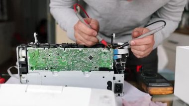 Adam servis merkezindeki bilgisayar parçalarını tamir ediyor. Laboratuvarda onarım ve onarım servisi. Elektronik tamir hizmeti konsepti. Teknisyen elleri dijital çokölçer kullanarak kontrol ediyor..