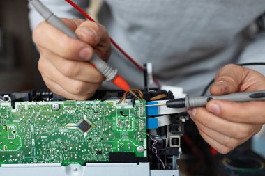 Adam servis merkezindeki bilgisayar parçalarını tamir ediyor. Laboratuvarda onarım ve onarım servisi. Elektronik tamir hizmeti konsepti. Teknisyen elleri dijital çokölçer kullanarak kontrol ediyor..