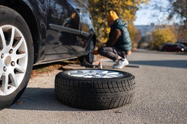 Young man changing tire of car on roadside, closeup