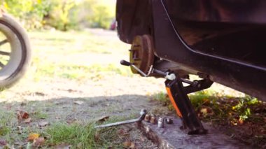 İş eldiveni giyen adam Jack 'i direksiyon değiştirmek için aracın altına yerleştiriyor. Erkek sürücü araba kaldırmak için doğru konumda lastik ayarlama aracı değiştirmeye çalışır