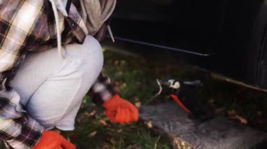 İş eldiveni takan kadın, Jack 'i direksiyon değiştirmek için aracın altına yerleştiriyor. Kadın sürücü araba kaldırmak için doğru konumda lastik ayarlama aracı değiştirmeye çalışır