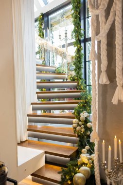 Dairedeki ahşap merdivenler Noel ağacı dallarıyla süslenmiş. Merdivenler Noel süsleri ve çelenklerle süslenmiş..