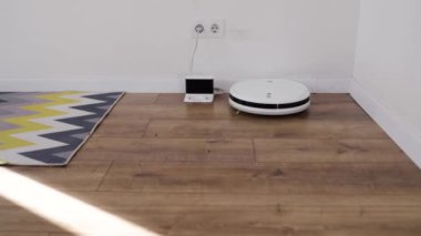 Şarj istasyonunun ahşap zemininde modern bir oturma odasında robot süpürgesi. 