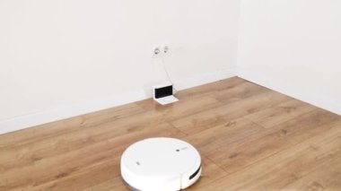 Beyaz robotik elektrikli süpürge temizliği bitirir ve şarj istasyonuna gider. Robot elektrikli süpürge odadaki zemini temizliyor. Ev kadınlarının temizlik yapmasına yardımcı olan modern teknolojiler.