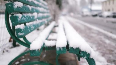 Bulutlu bir günde park bankına düşen kar manzarasını kapat