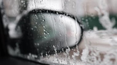 Karlı bir yolda araba sürerken arabanın içinde dikiz aynasından görüntüler. Yan cama yağmur damlaları ve arabanın aynası. Bir kış günü seyahat ederken.