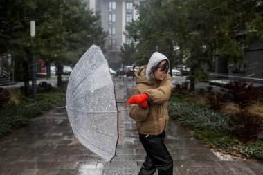 Kışın şiddetli rüzgar ve kar altında şemsiyesini tutmaya çalışan Asyalı kadın..