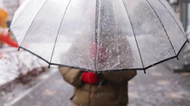 Kışlık ceketli, şemsiyeli genç bir Asyalı kadın kar tatilinde küçük bir kasaba caddesinde yürüyor..