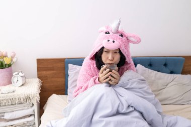 Kapüşonlu bir kadın ve soğuk odada sıcak mavi battaniyeye sarılı bir atkı. Soğuk mevsim ısınma mevsimi başladıkça başlar. Sıcaklık ve rahatlık ararken kendini iyi hissetmiyor..