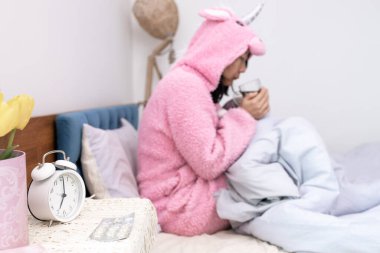 Gribe dayanan Asyalı bir dişi evde teselli arıyor. Elinde bir bardakla, soğuk yatak odasındaki yorganın altında titreyerek ilacı içiyor ve mevsimsel hastalığın acı gerçekliğinin bir örneği oluyor..