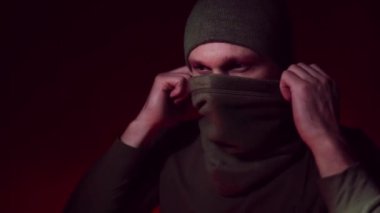 Genç, ciddi bir erkek Ukrayna askerinin portresi taktik yüz maskesi takıyor ve karanlık arka planda dikiliyor..