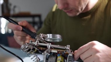 Atölyedeki elektronik cihazın devre levhasını lehimleyen erkek teknisyen ellerini kapat. Tahtadaki mikroçipleri değiştir ve onar..