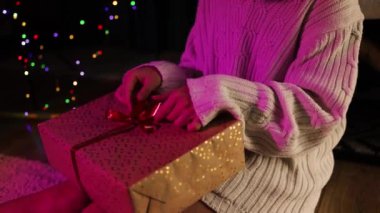 Hediye kutusunu açarken Noel ağacının altında oturan kadın hediyesinden memnun görünüyor. Noel ve Yeni Yıl Kutlaması Noel ağacı, hediyeler ve hediye kutuları. 