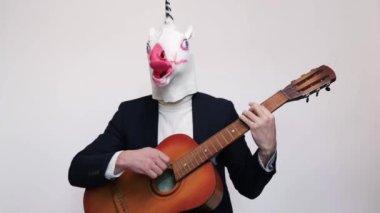 Takım elbiseli, at kafası atlayan ve beyaz arka planda gitar çalan komik bir genç. Dikey video.