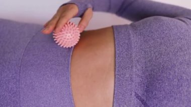 Asyalı kadın, karın kaslarının üzerinde dikenli bir top yuvarlıyor. Cilt üzerinde pembe dikenli top. Kas masajı. Dikey video.