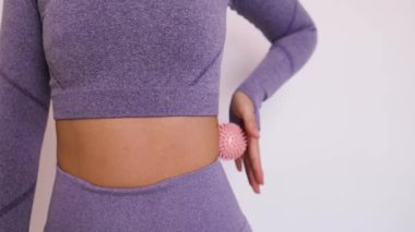 Asyalı bir kadın vücudunun yan kasları boyunca dikenli bir top yuvarlıyor. Cilt üzerinde pembe dikenli top var. Kas masajı.