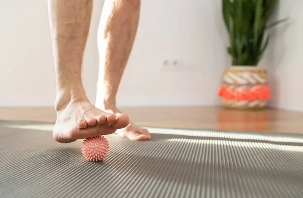 Düz taban, topla masaj yapıyor. Ayak masajı için çivili top kullanan bir adam evdeki kan dolaşımını iyileştirmek için fiziksel egzersiz yapıyor.. 