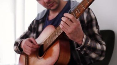 Gitar çalıyorum. Akustik gitar tıngırdatıyorum. Müzisyen müzik çalar. Erkek parmakları arabulucuyu tutuyor. Karanlık odada gitar çalan bir adam eli. Tanımlanamayan kişi prova yapıyor, fretboard yakın plan.