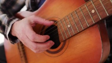 Gitar çalıyorum. Akustik gitar tıngırdatıyorum. Müzisyen müzik çalar. Erkek parmakları arabulucuyu tutuyor. Karanlık odada gitar çalan bir adam eli. Tanımlanamayan kişi prova yapıyor, fretboard yakın plan.