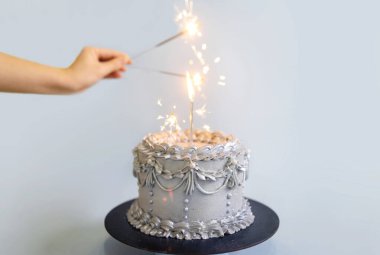 Mumlu gümüş bir doğum günü pastası ve mavi arka planda kutlama maytapları.