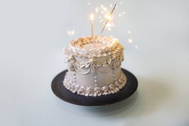 Mumlu gümüş bir doğum günü pastası ve mavi arka planda kutlama maytapları.