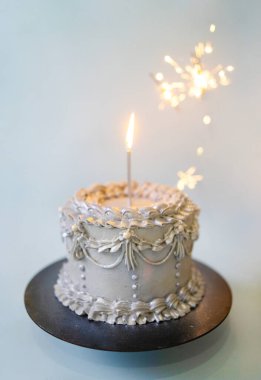 Mumlu gümüş bir doğum günü pastası ve mavi arka planda kutlama maytapları.