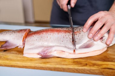 Şef eller somon filetosunu mutfaktaki tahta masada bıçakla kesti. Sağlıklı beslenme için limonlu kırmızı omega balığı pişiren adam.