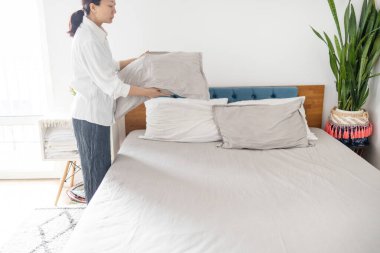 Otel hizmetçisi otel odasını temizler ve yatağı toplar..