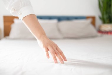 El yumuşaklığı doğal kumaşa dokunur. Ortopedik şilteye dokunan kadın, yakın plan. Yumuşak bir yorganın üzerinde.