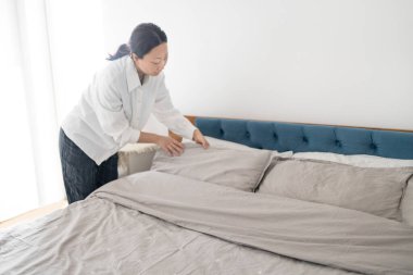 Otel hizmetçisi otel odasını temizler ve yatağı toplar..