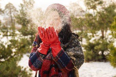 Mutlu Asyalı kadın, kar yağışlı kış gününde ellerine kar alıp üfledi. Kar taneleri içinde saç ve şapka.