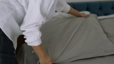 Yatağı yapan kadın, yatak odasındaki yumuşak yastıkları kabartıyor. Genç Asyalı kadın yatak odasını temizler ve yatağını toplar..