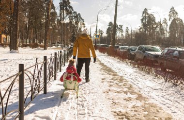 Genç baba güneşli bir günde karlı kış parkında kızak taşıyor..