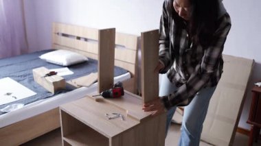Mobilya montajı. Kadın komodini monte ediyor. İşçi elektrikli matkap kullanıyor. Yakın plan. El ve çerçeve.